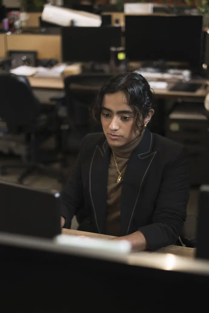 A trans man deep in thought while working at a desk in an office. 